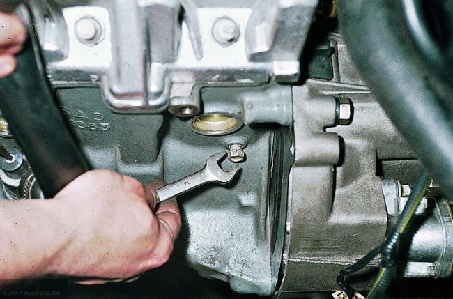 Пробка слива охлаждающей жидкости с блока двигателя автомобиля ВАЗ-2110 и ключ на 13 в руке механика